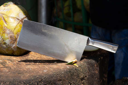 Stainless steel cleaver knife for coconuts stuck in an old wooden chopping board.の写真素材
