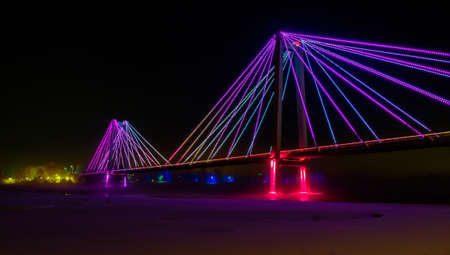 Night illumination of the foot Vinogradovsky bridge through the Yenisei river on Tatyshev island in Krasnoyarsk, Russia. Low light shooting.の写真素材