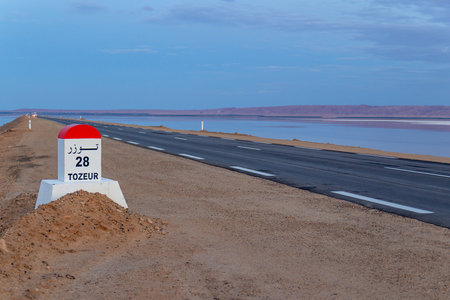 Milestone post on the Tozeur highway written in French and Arabic. Road passes through salt lake of Chott el Djerid, Tunisia.の写真素材