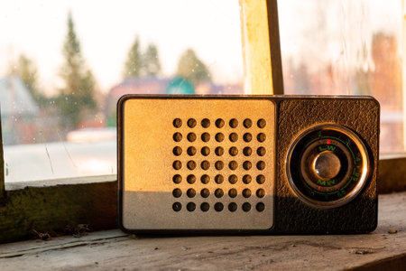 Vintage portable radio receiver stands on a dusty windowsill against the background of an unwashed...