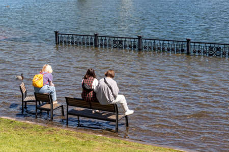 Krasnoyarsk, Russia - June 1, 2021: girls sit on benches on a flooded city embankment. Flooding of Yenisei River in spring during melting a lot of snow. Natural disasterのeditorial素材