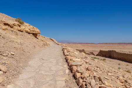 Cobblestone road on the hillside in the ancient Ait Benhaddou Kasbah near Ouarzazate city Morocco, North Africa. Desert landscape with empty dusty trail on blue sky backgroundの写真素材