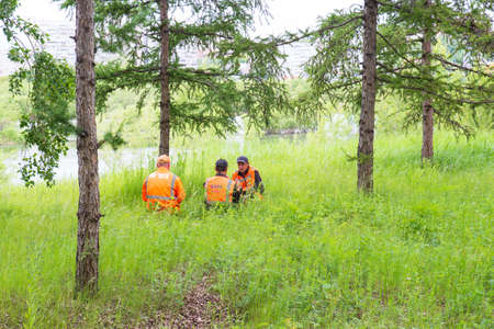 Krasnoyarsk, Russia - June 28, 2021: Workers in orange service suits rests on lawn. A city utility...