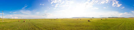 Russian summer panoramic landscape with sunny green meadows with mown hay, haystacks and awe sky...