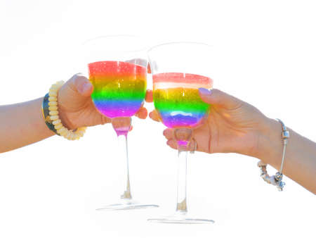 Happy lgbt-couple have a romantic date with rainbow cocktails. Pair of women hold glasses of wine and clink glasses. Cheers to happily ever after. Holiday greetings background. High-key lightingの写真素材