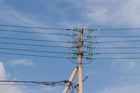 Concrete electrical power line utility pole with green glass insulators and six parallel connected overhead wires against blue sky background.の写真素材