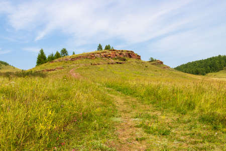 Landscape with a narrow path among the summer green steppe leading to the top of a hill with Sulek Pisanitsa in the Republic of Khakassia, Russia. Monument of ancient culture.の写真素材