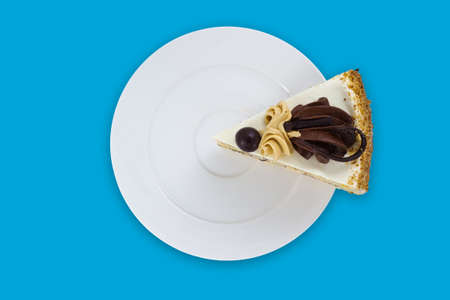 A slice of cake decorated with buttercream and chocolate on a white plate on cyan background. Top viewの写真素材