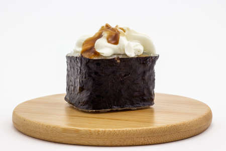 Still life with sushi roll on a round wooden plate isolated on white background. Japanese roll garnished with cream cheese and sauce. Asian cuisineの写真素材