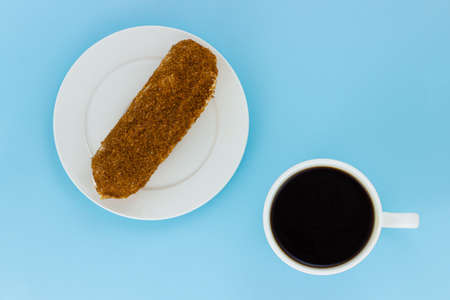 Eclair decorated with sweet crumb in a white plate and cup of black coffee isolated on a pale blue...