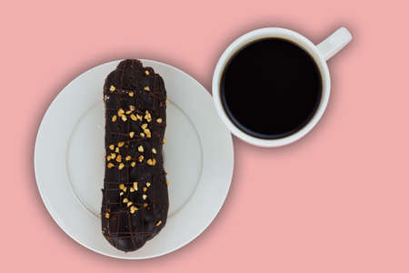 Eclair decorated with dark chocolate and nuts in a white plate and cup of black coffee isolated on a pale pink background. Still life with french pastries and coffee. Top viewの写真素材