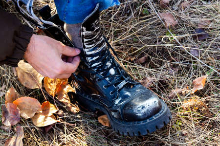 Man ties a high massive leather shoe on the autumn forest trailの写真素材