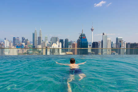 Kuala Lumpur, Malaysia - March 16, 2019: Man in infinity swimming pool with panoramic view Kuala Lumpur city, Malaysia.のeditorial素材