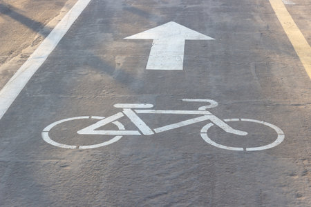 Signs of Bike and Arrow on the asphalt. Sidewalk for cyclists. White road markings on pavement. Bike lane symbol. Indicates the direction of movementの写真素材