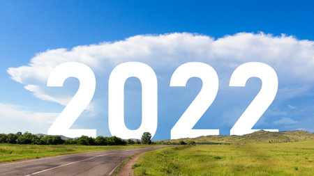 Inscription 2022 year among the sunny nature landscape. Empty asphalt road leading forward to happy...