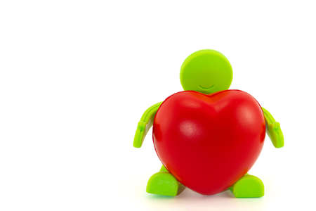 A sitting toy green man with smile holds a big red heart in his hands. Isolated on white background with copy space. Concept Give your love and Valentine day holidayの写真素材