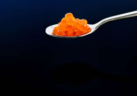 Close-up little spoon with red caviar on black background. Salted salmon caviar.の写真素材