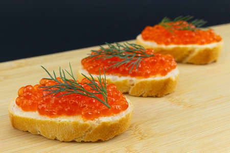Set of red caviar sandwichs on wooden board and black background. Salted salmon caviar on wheat bread with fresh fennel.の写真素材