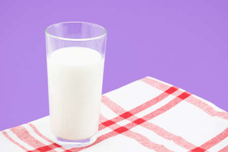 Full glass of milk on a red and white checkered linen napkin on a purple background and copy space. Healthy diet and source of calciumの写真素材