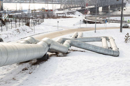Industrial urban winter landscape with huge steam pipes of the central boiler plant with heating pipes. Urban water communications in winter. Heating season in Russia.の写真素材