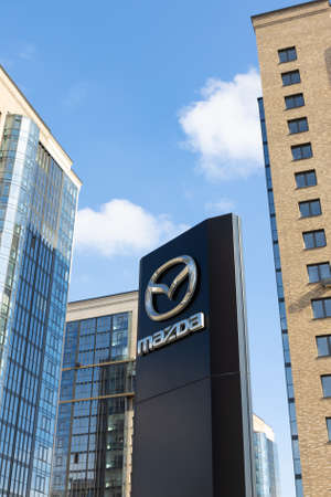Krasnoyarsk, Russia - March 13, 2022: Mazda brand logo on against residential buildings. Dealership...