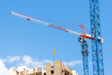 Construction cranes on the construction site of residential building against the blue sky....