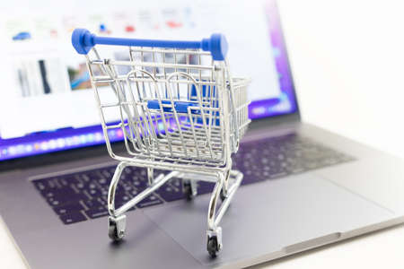 Mini shopping trolley on blurred laptop background. Concept online shopping and e-commerce....