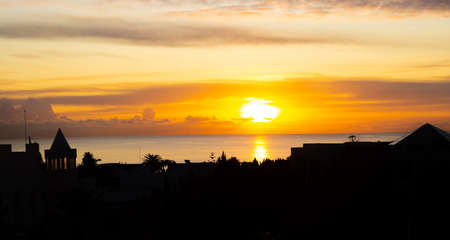 Orange sunset over the sea with a black coastline silhouetteの写真素材