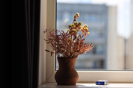 Still life of a earthenware jug with dried flowers and a pack of cigarettes on the windowsillの写真素材