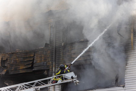 Alone firefighter on ladder in rescue operation extinguishing strong fire with from a fire fighting...