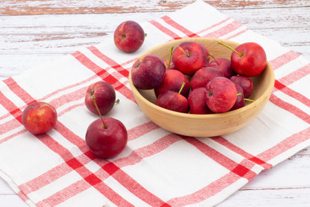 Still life with fresh small apples in wooden bowl on a red and white checkered linen napkin. Wild red crabapples in bowl on wooden tablの写真素材