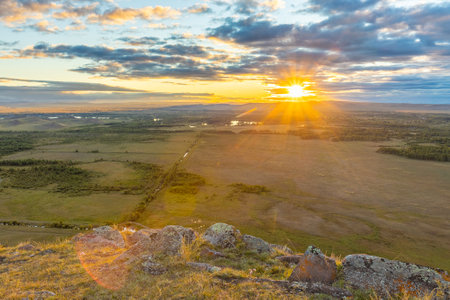 Golden sunset over the autumn Khakas steppe. Top view from the mountain range to the valley. The bright sun shines through the clouds of the evening skyの写真素材