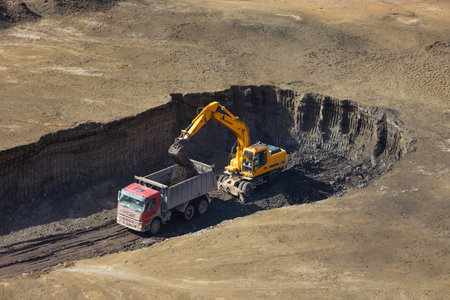 Krasnoyarsk, Russia - September 8, 2022: Excavator loading a dump heavy truck with soil during quarrying. Heavy machinery working in the quarry. Excavator digs the ground. top viewのeditorial素材