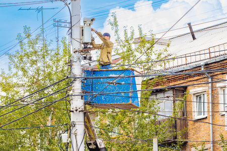 Technician in a car cradle connects a surveillance camera on an electric pole. Installation urban work on CCTV on field. Connecting power cordsの写真素材