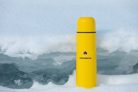 Krasnoyarsk, Russia - February 4, 2023: Yellow thermos with Rosneft logo in the white snow background. PJSC Rosneft Oil Company is a Russian oil and gas companyのeditorial素材