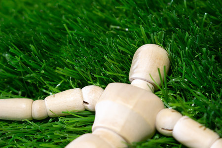A wooden man puppet lies on the green grass with his arms outstretched. Wooden mannequin among green grass.の写真素材