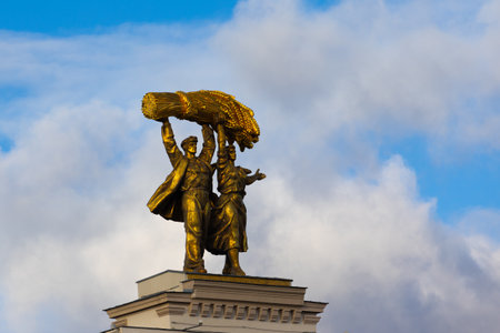 Moscow, Russia - November 13, 2022: Golden sculpture Tractor driver and collective farmer against the blue cloudy sky. The statue is installed on the arch of the main entrance to VDNKh.のeditorial素材