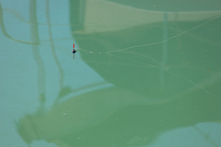 Fishing float with line on the water surface. Blurred shadows on the waterの写真素材