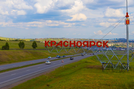 Krasnoyarsk, Russia - August 1, 2022: red inscription Krasnoyarsk against highway and far cityscape. Welcome road sing with city coat of arms installed on at the entrance to the Krasnoyarsk cityのeditorial素材