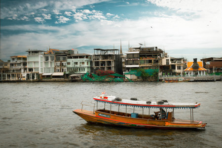 Bangkok, Thailand - December 29, 2023: Empty old wooden boat against mini-hotels and residential buildings on the riverbanks of the Chao Phraya River in Bangkok, Thailand. Real local life in Asiaのeditorial素材