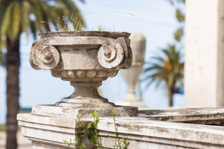 Old white stone outdoor flowerpot with growing weeds against blurred background. Vase adorned the now abandoned railway station in old Gagra town , Abkhazia, Georgiaの写真素材