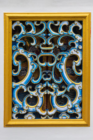 Close-up of blue-white carved oriental ornament on a window with a gold frame on a white wall of a...