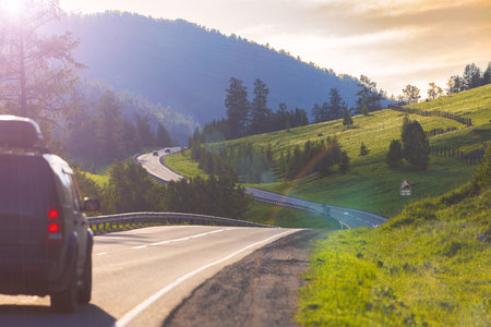 Sunny summer mountains landscape with winding asphalt road with cars driving in the Altai Republic, Russia. Russian route R256 or Chuya Highway at Altai. New asphalt pavement with road markingsの写真素材