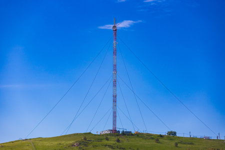 Red and white cellular base station with guy ropes is installed on top of a hill. Mobile communication tower against blue sky backgroundの写真素材