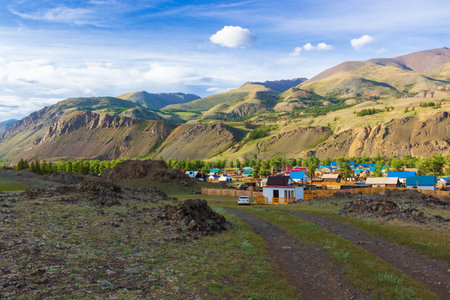 View of the outskirts of the village of Chagan-Uzun at the foot of the Altai Mountains in the Altai Republic, Russia. Summer landscape with mountains and small village housesの写真素材