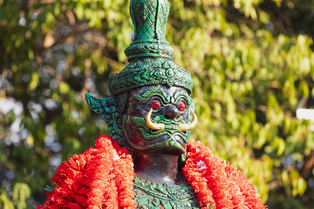 Portrait of green Dvarapala spirit decorated with a red flower garland in Buddhist temple at Pattaya, Thailand. Dvarapala or Dvarapalaka is a door or gate guardian at East Asiaの写真素材