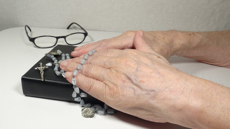 Elderly woman's hands with rosary beads, bible  and glassesの写真素材