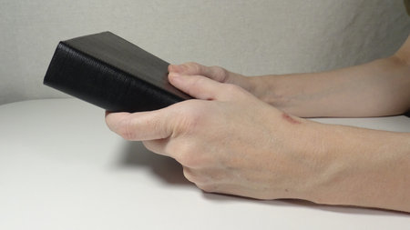 Female hands holding a black leather bible on a white table, close upの写真素材