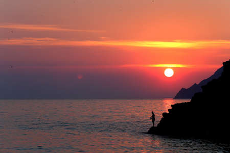 Sunset on sea with man silhouette and sun reflection on the water. Italyの写真素材