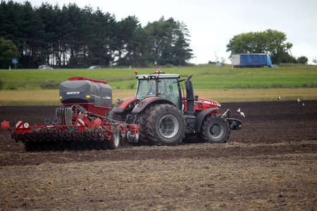 Farmer plowing the field Cultivating tractor in the field Red farm tractor with a plow in a farm...